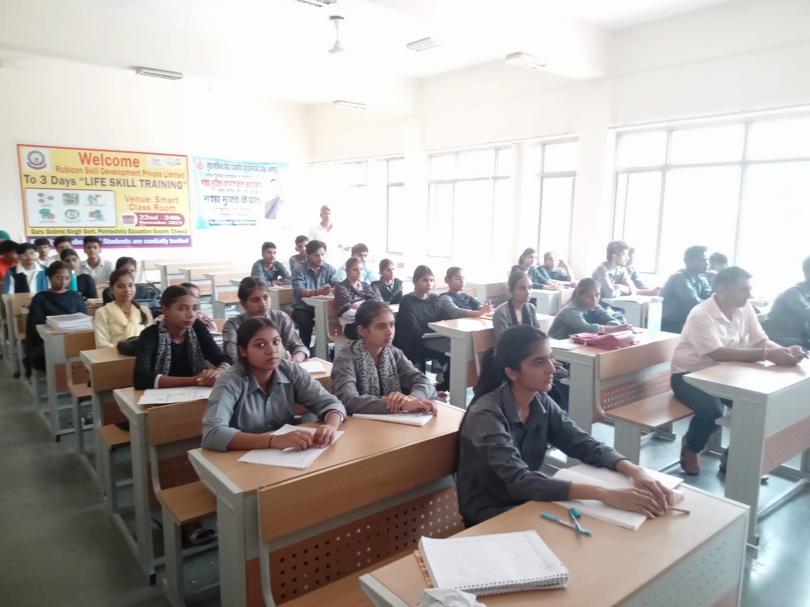 Students seated at desks facing the front of a classroom, the front row taking notes during a session.