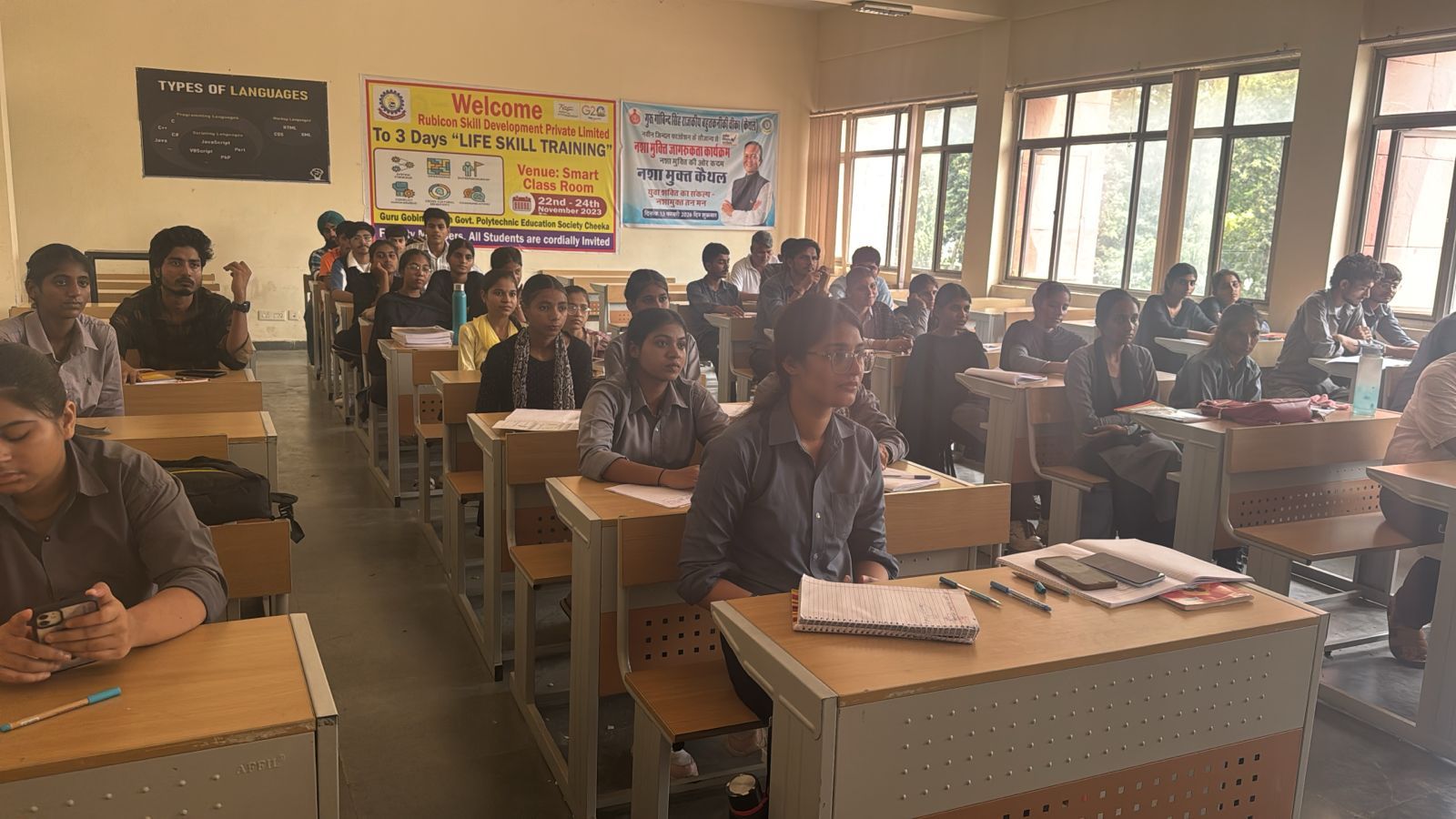 A wide, bright classroom with students at desks during a life-skills training session.