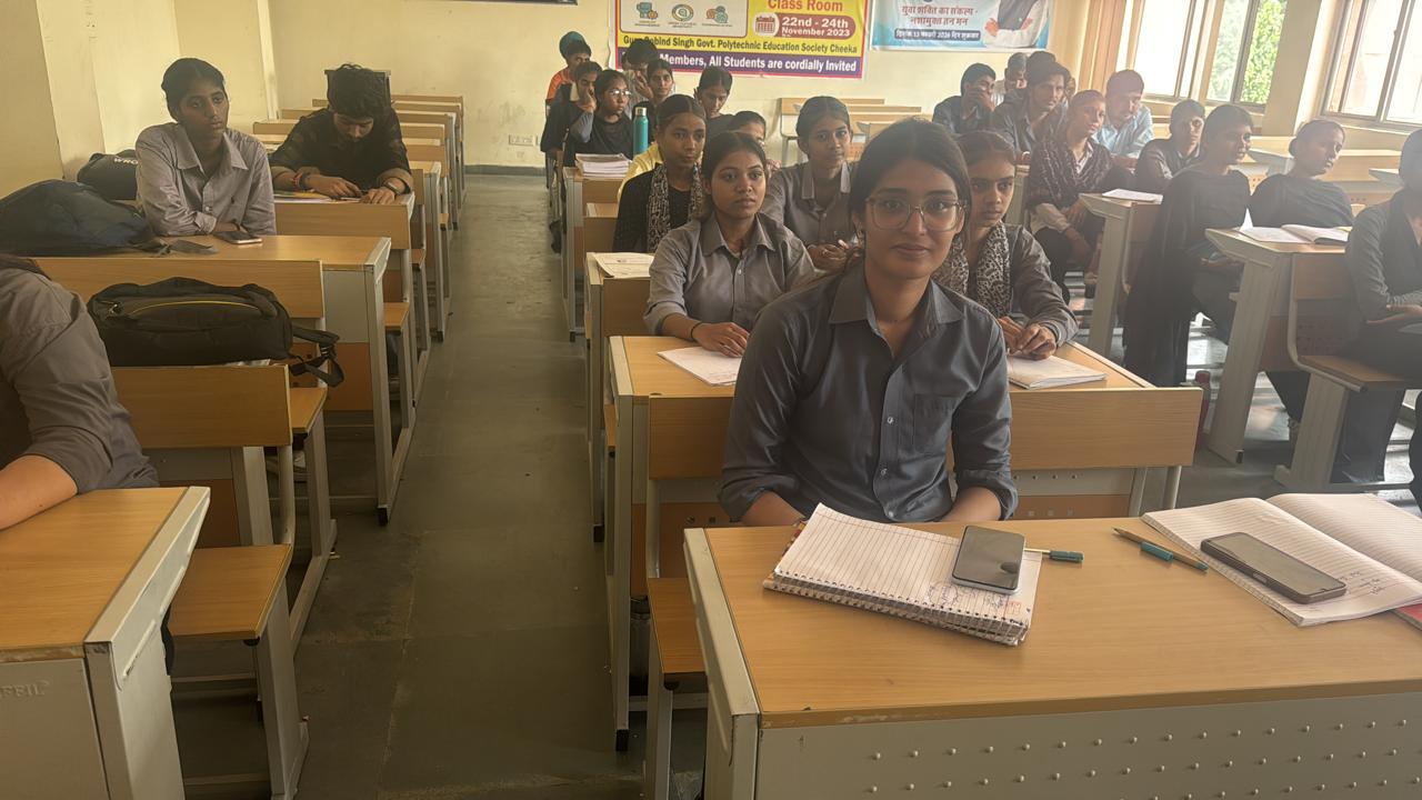 A student at her desk with an open notebook, classmates seated at desks behind her.