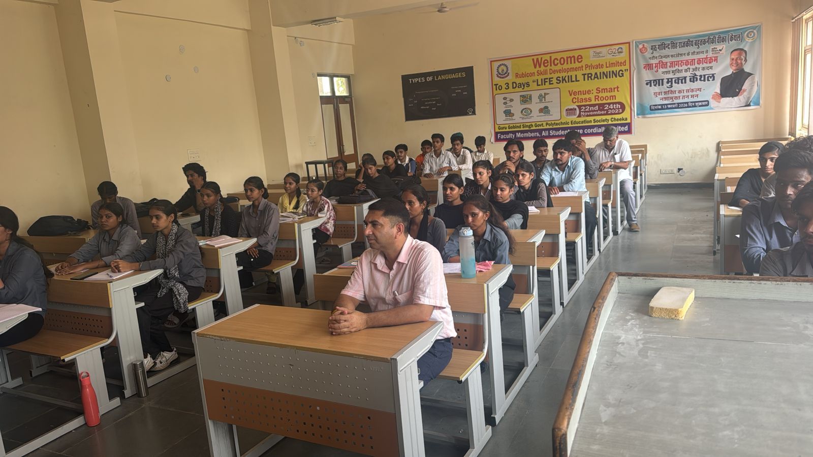 A faculty member seated among students in a wide classroom during a session.